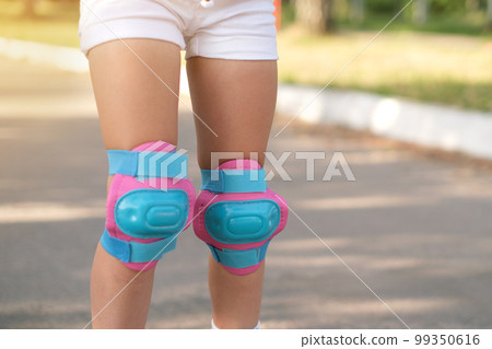 Close-up of pink and blue protective knee pads on the girl's legs. Protection in case of falls and accidents 99350616