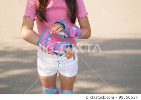Close-up of a girl fastening Velcro on protective gloves before roller skating and skateboarding Close-up of a girl fastening Velcro on protective gloves before roller skating and skateboarding 99350617
