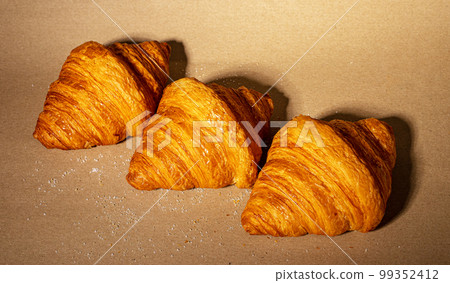 Three fresh twisted croissants on craft paper background. French bakery row composition Three fresh twisted croissants on craft paper background. French bakery row composition 99352412