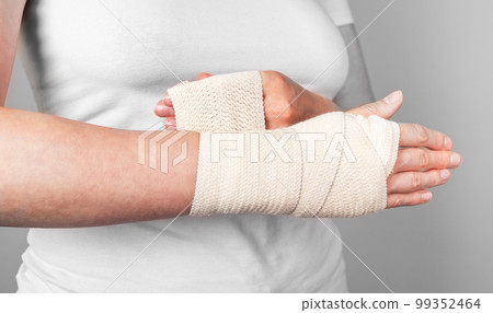 Woman wrapping compression bandage around sprained wrist to reduce pain and swelling. Arm injury. Health care concept. 99352464