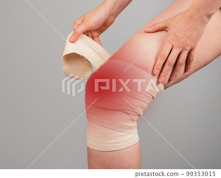 Woman wrapping elastic bandage around painful knee to relieve pain or prevent injury. Female suffering from leg discomfort. Sprained ligaments, torn cartilage. 99353015