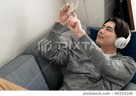 坐在沙發上看智能手機的男人 99354186