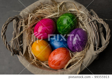 Multi-colored painted Easter eggs in a basket on a dark stone background. Happy Easter holiday card or banner. Multi-colored painted Easter eggs in a basket on a dark stone background. Happy Easter holiday card or banner. 99355913