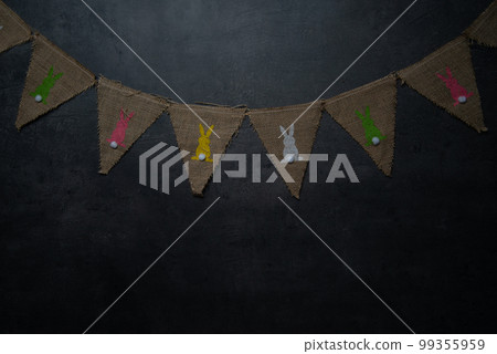 Linen flags with Easter bunnies on a dark stone background.Happy Easter holiday card or banner. Copy space. Linen flags with Easter bunnies on a dark stone background.Happy Easter holiday card or banner. Copy space. 99355959
