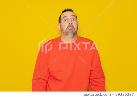 Bearded latino man wearing a red sweater with expression of doubt and confusion shrugging shoulders isolated over yellow background. 99356387