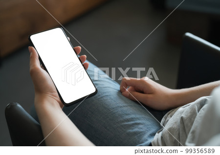 Young woman sitting in chair and holding smartphone with white screen Young woman sitting in chair and holding smartphone with white screen 99356589