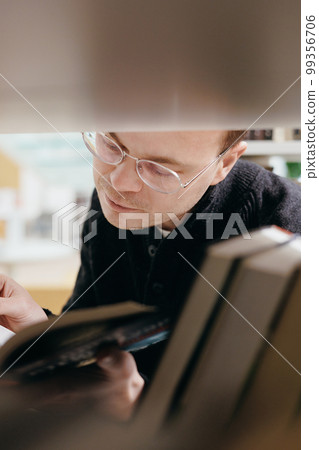 confident man chooses books on shelf in library, education at university or independently online, confident man chooses books on shelf in library, education at university or independently online, 99356706