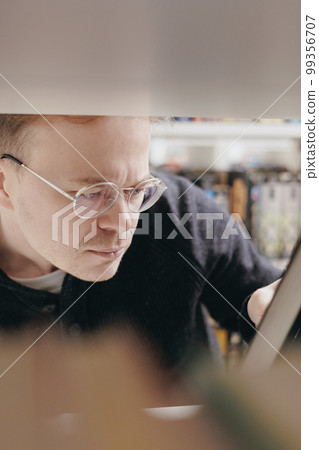 confident man chooses books on shelf in library, education at university or independently online, confident man chooses books on shelf in library, education at university or independently online, 99356707
