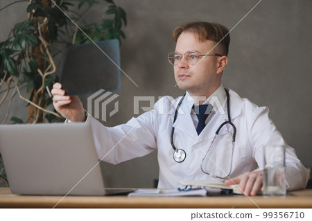focused male doctor in white coat looks at X-ray and diagnoses patient. focused male doctor in white coat looks at X-ray and diagnoses patient. 99356710