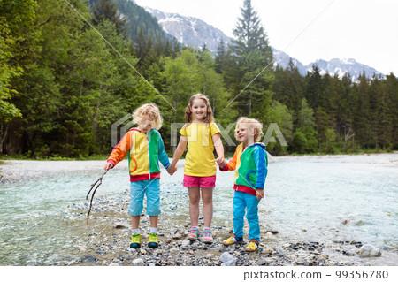Child hiking in mountains. Kids at river shore. 99356780