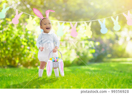 Baby with bunny ears on garden Easter egg hunt 99356928