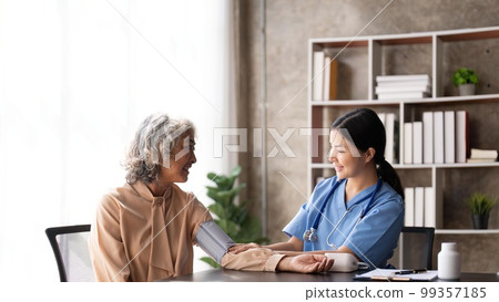 Nurse measuring blood pressure of senior woman. Smiling to each other. Doctor checking elderly woman's blood pressure 99357185