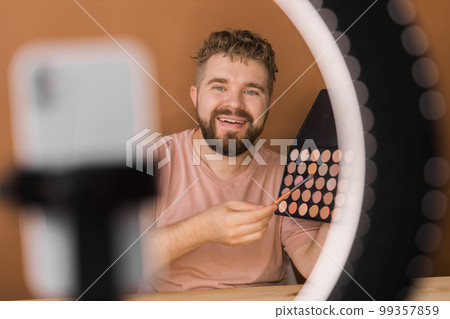 Man talking on cosmetics holding a makeup tools while recording his video. Guy making video for his blog on cosmetic product 99357859