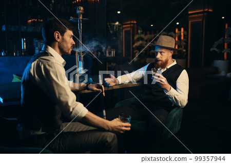 Guys having serious conversation while sitting face to face at hookah bar 99357944