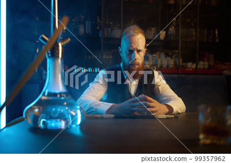 Portrait of lonely bearded man smoking hookah and drinking brandy Portrait of lonely bearded man smoking hookah and drinking brandy 99357962