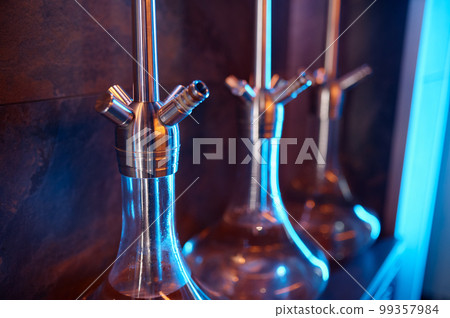 Closeup hookahs with glass flask and metal bowl selective focus Closeup hookahs with glass flask and metal bowl selective focus 99357984