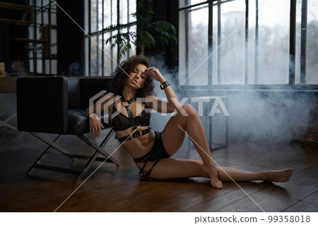 Woman in erotic underwear sitting on wooden floor and leaning on chair Woman in erotic underwear sitting on wooden floor and leaning on chair 99358018
