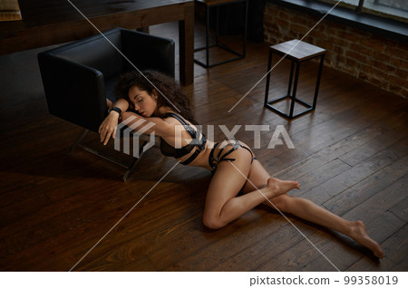 Woman in erotic underwear lying on wooden floor and leaning on chair Woman in erotic underwear lying on wooden floor and leaning on chair 99358019
