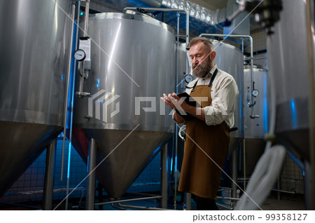 Handsome bearded man brewer inside modern beer factory around steel tanks 99358127