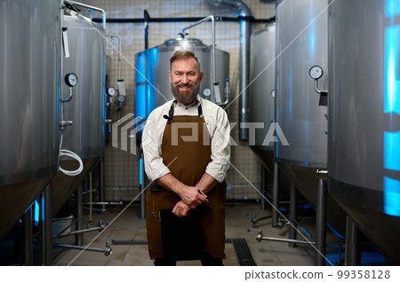 Portrait of smiling brewer man in apron standing among distillery vats 99358128
