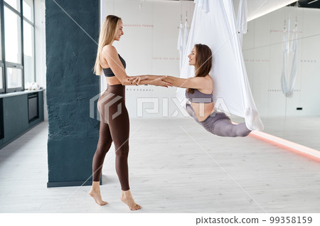 Woman training leg-split with fly yoga instructor at fitness gym 99358159