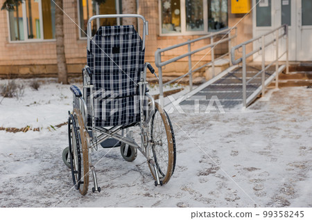 Empty wheelchair in the hospital on the ramp. Wheelchair close-up. Children's wheelchair Empty wheelchair in the hospital on the ramp. Wheelchair close-up. Children's wheelchair 99358245