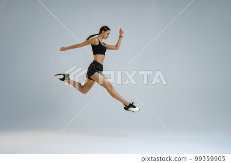 Sporty girl jumping doing split leap in air with joyful expression. Flexible and weightless concept Sporty girl jumping doing split leap in air with joyful expression. Flexible and weightless concept 99359905