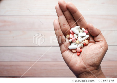 man's hand with medicine spilled out of the pill container  99362576