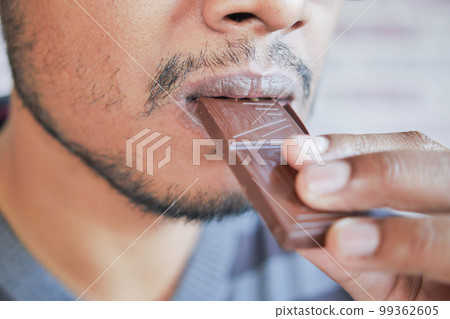 young man eating dark chocolate close up young man eating dark chocolate close up 99362605