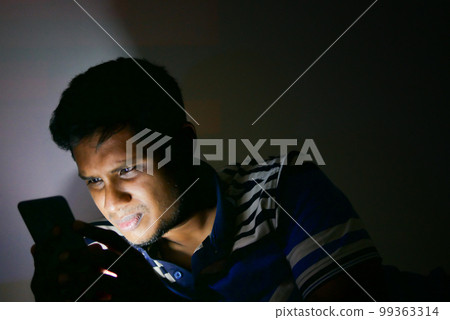 young man sitting on bed using smart phone at night young man sitting on bed using smart phone at night 99363314
