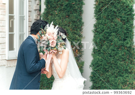 A bride and groom kissing while holding a bouquet in the garden of the wedding hall at the wedding ceremony (garden wedding) 99363692