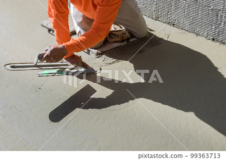 Worker plasters wet cement concrete floor using trowel after pouring concrete in floor 99363713