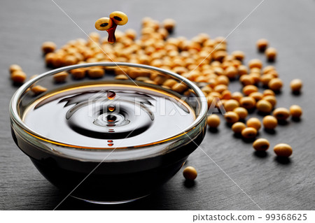 soy sauce drop falling from flying soybeans in glass bowl and created splash on black stone background 99368625