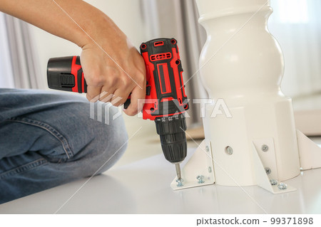 man assembling white table furniture at home using cordless screwdriver 99371898
