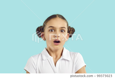 Surprised little Caucasian girl teenager opening mouth in amazement looks at camera stands in studio 99373023