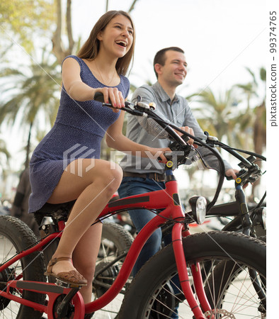 couple guy with a girl ride bicycles with thick wheels in the summer along the promenade couple guy with a girl ride bicycles with thick wheels in the summer along the promenade 99374765