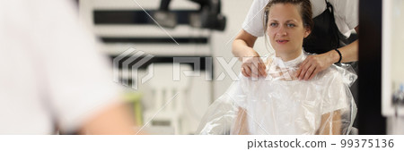 Female hairdresser puts paper collar bag around woman neck to protect clothes she cuts hair indoors Female hairdresser puts paper collar bag around woman neck to protect clothes she cuts hair indoors 99375136
