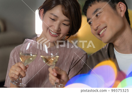 A young couple toasting with white wine in the living room at night 99375325