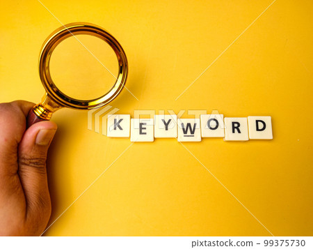 Hand holding magnifying glass with the word KEYWORD on yellow background 99375730