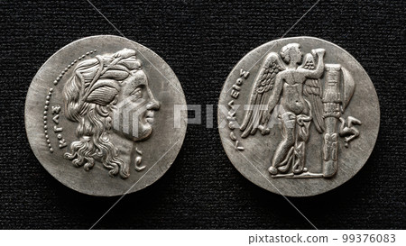 Ancient Greek coin, macro view of money with human portrait and winged god 99376083