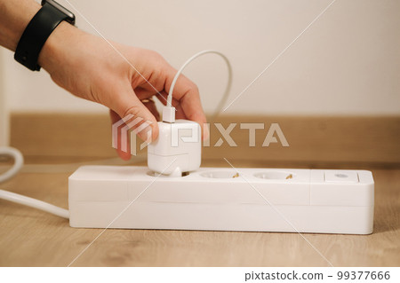 Human hand puts the charger into the extension cord. White cable connector Human hand puts the charger into the extension cord. White cable connector 99377666