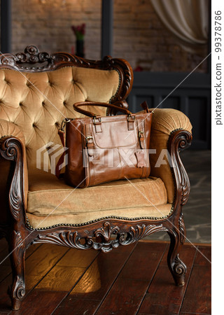 close-up photo of brown leather bag on a yellow velor vintage armchair. 99378786