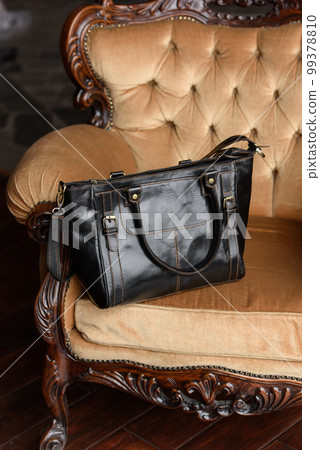 close-up photo of black leather bag on a yellow velor vintage armchair. 99378810
