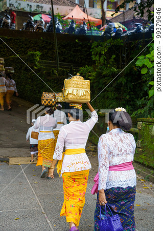 A Balinese woman walks with a basket of offerings on her head (Bali, Indonesia) 99379646