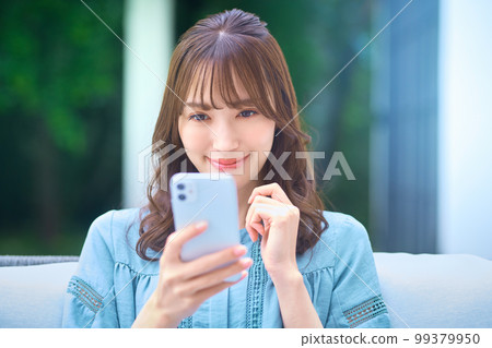 Young woman wearing glasses operating a smartphone in her garden at home 99379950