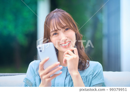 Young woman wearing glasses operating a smartphone in her garden at home 99379951