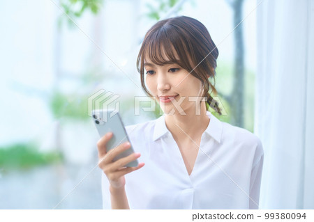 A young housewife operating a smartphone in the living room A young housewife operating a smartphone in the living room 99380094