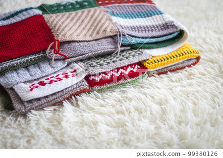 Knitted warm blanket on bed. Woolen plaid on white sofa. Patchwork plaid. Cozy room interior. Hygge style in bedroom. Knitting hobby. Winter coziness concept. Knitting crochet. Scandinavian needlework 99380126