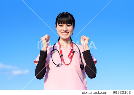 A female nurse wearing a scrub standing against the blue sky, a medical worker, a doctor, and a fist pump A female nurse wearing a scrub standing against the blue sky, a medical worker, a doctor, and a fist pump 99380308