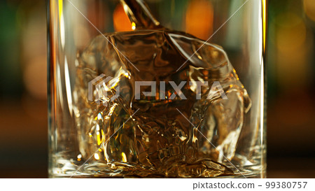 Detail of pouring whiskey into glass with ice cubes. 99380757